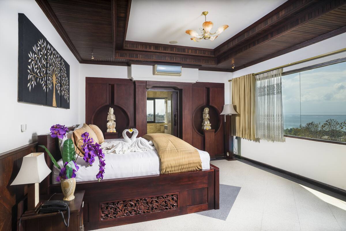 A spacious bedroom with a large bed, a view of the sea, and a chandelier.