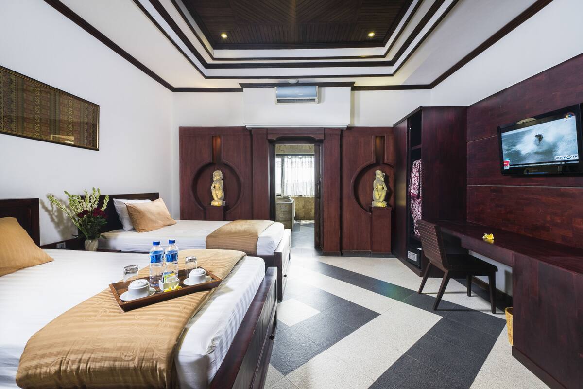 A hotel room with two beds, a TV, a desk, and a reception area.