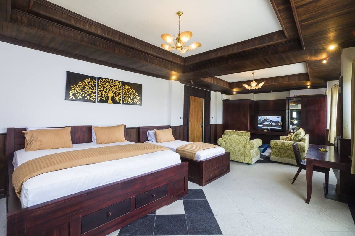 A hotel room with two beds, a sofa, a TV, and a wooden ceiling.