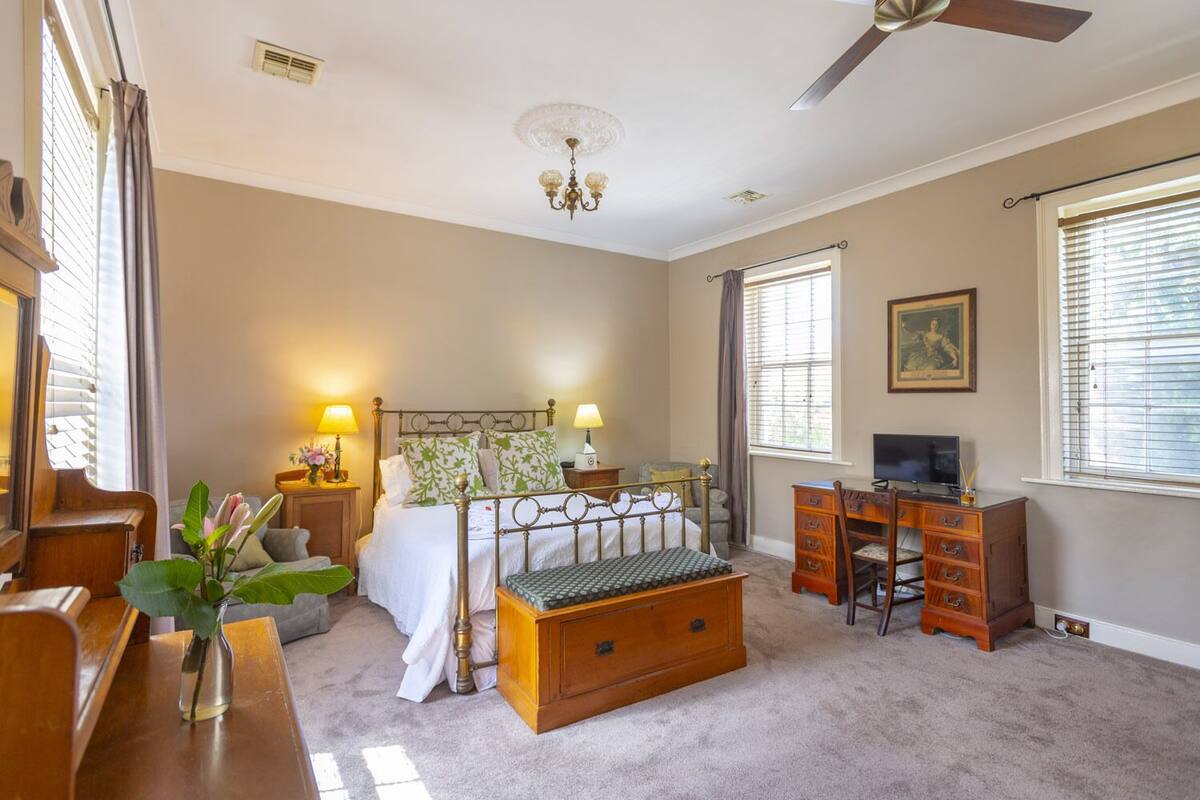 A bedroom with a bed, bedside tables, a desk, a television, and a ceiling fan.