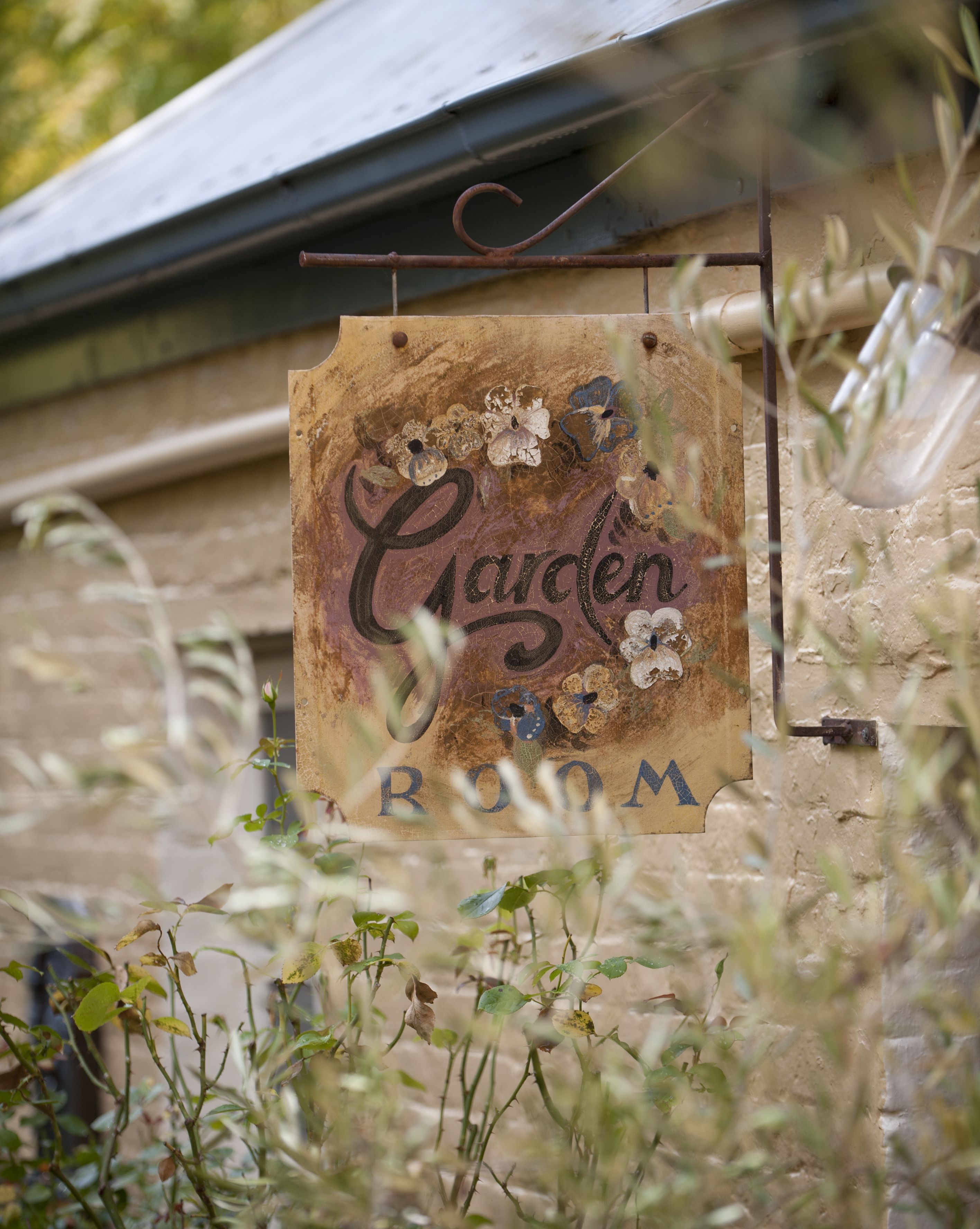 A rustic sign with the words "Garden Room" hanging on a metal structure.