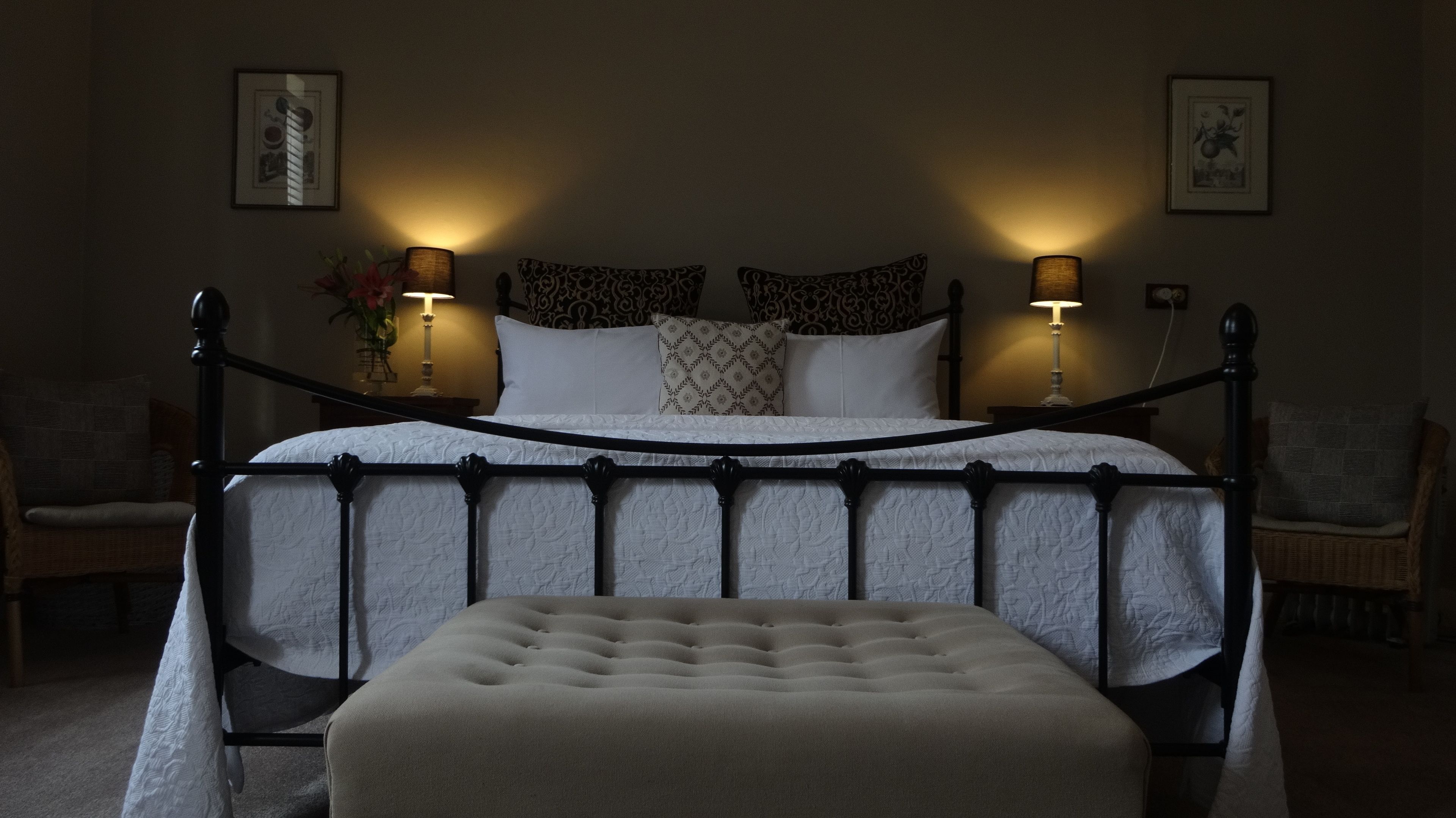 A neatly arranged bedroom with a four-poster bed, two bedside lamps, and a bedside table with a vase of flowers.