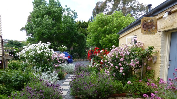 Ein Garten mit einem Kiesweg, der zu einem Gebäude führt, an dem ein Schild mit der Aufschrift 'Garden Room' hängt.