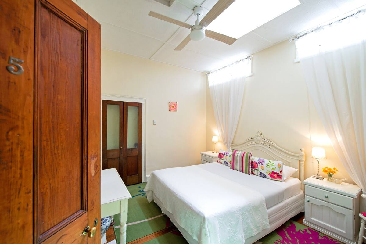A bedroom with a bed, nightstands, a wooden door, and a ceiling fan.