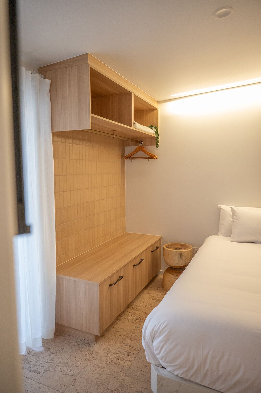 Un dormitorio con cama, armario de madera, mesita de noche y una planta colgante.
