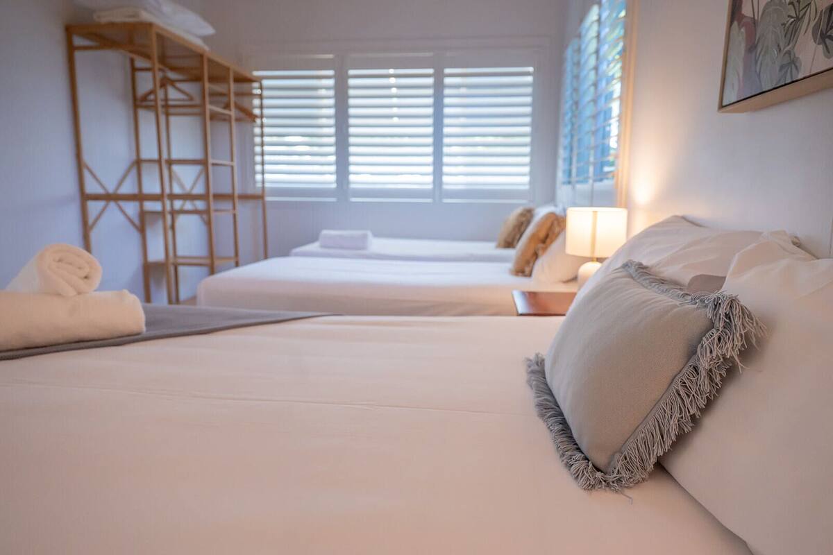 A hotel room with two beds, a wooden shelf unit, and a window with blinds.