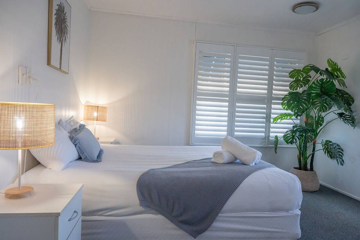 A neatly arranged bedroom with a bed, bedside lamp, and a potted plant.