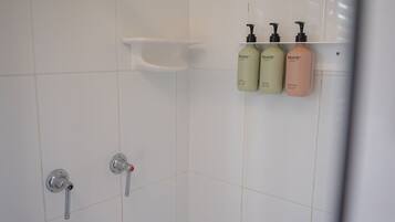 A bathroom with white tiles, a shower control panel, and three bottles of Sincerely shampoo and conditioner on a shelf.