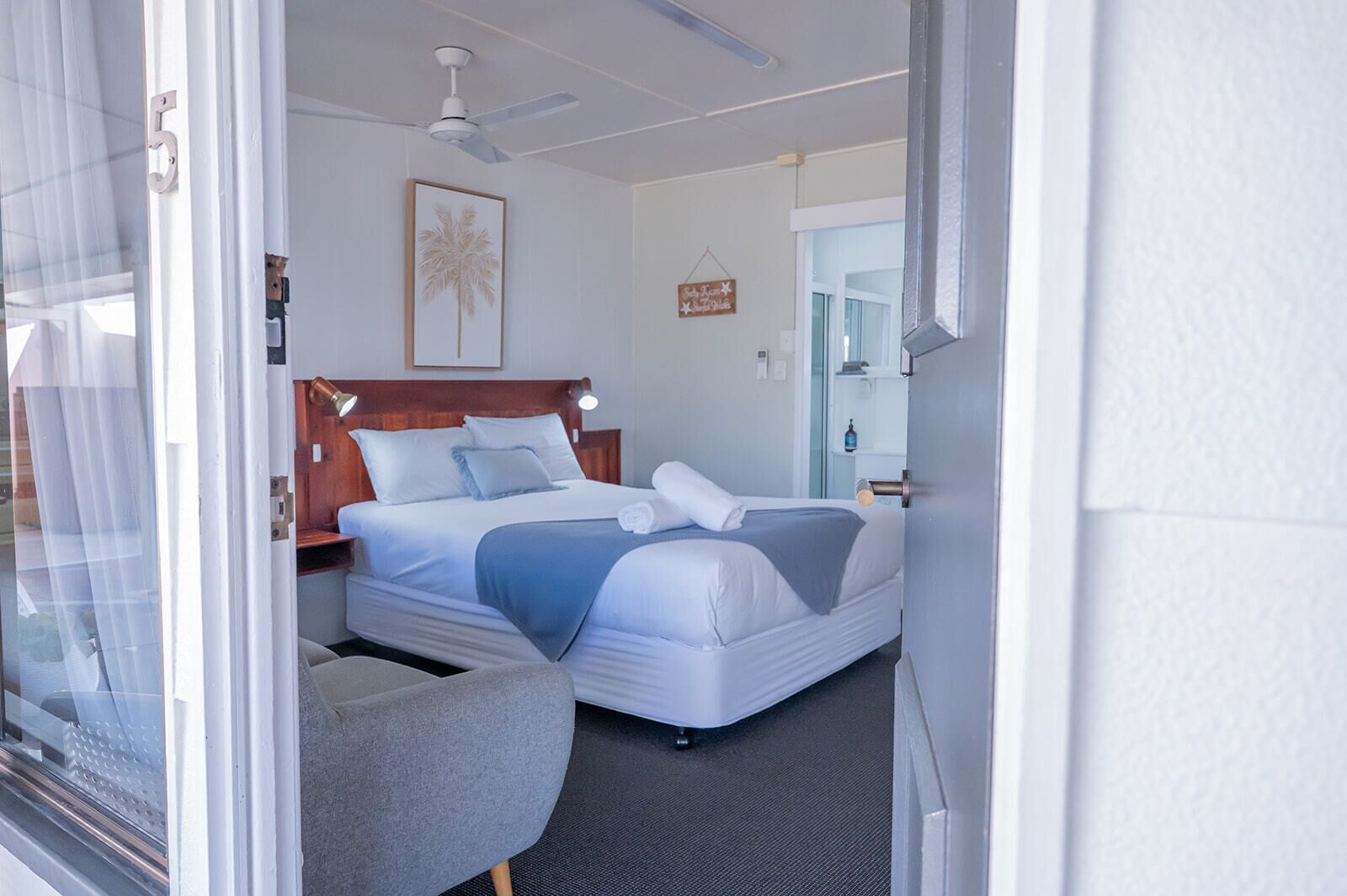 Une chambre d’hôtel avec un lit, une chaise, un ventilateur de plafond et une porte.