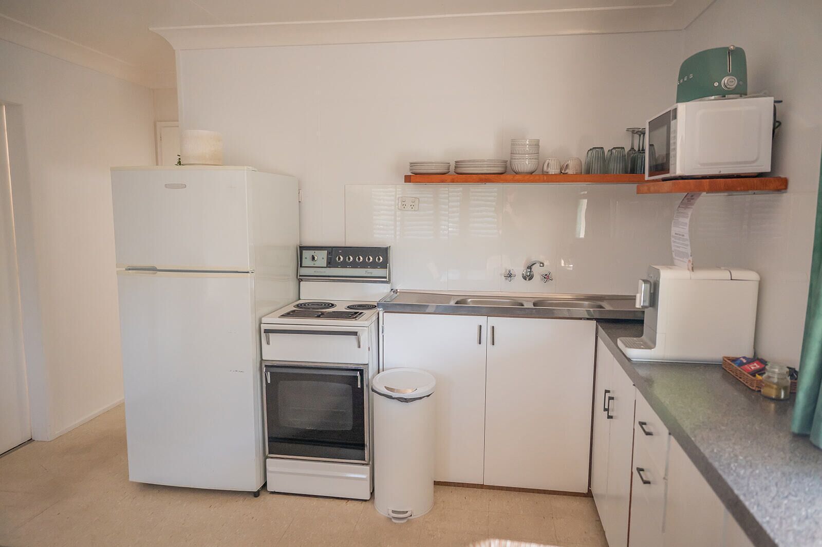 A compact kitchen with a refrigerator, stove, oven, sink, and a microwave on a shelf.