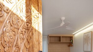 A bedroom with a bed, a wooden door with intricate carvings, a ceiling fan, and a framed picture on the wall. - Pacific Sun Bargara  (Bargara)