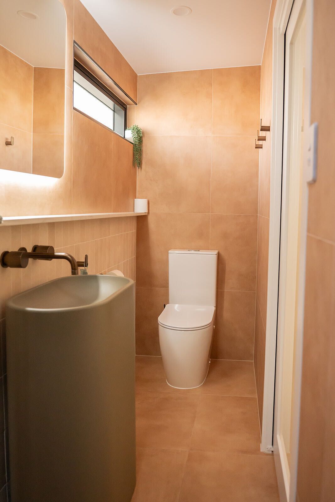 A bathroom with a large sink, toilet, and a small window with a plant.