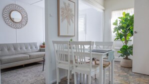 A modern living room with a white sofa, a dining table with white chairs, a framed artwork, and a large potted plant. - Pacific Sun Bargara  (Bargara)