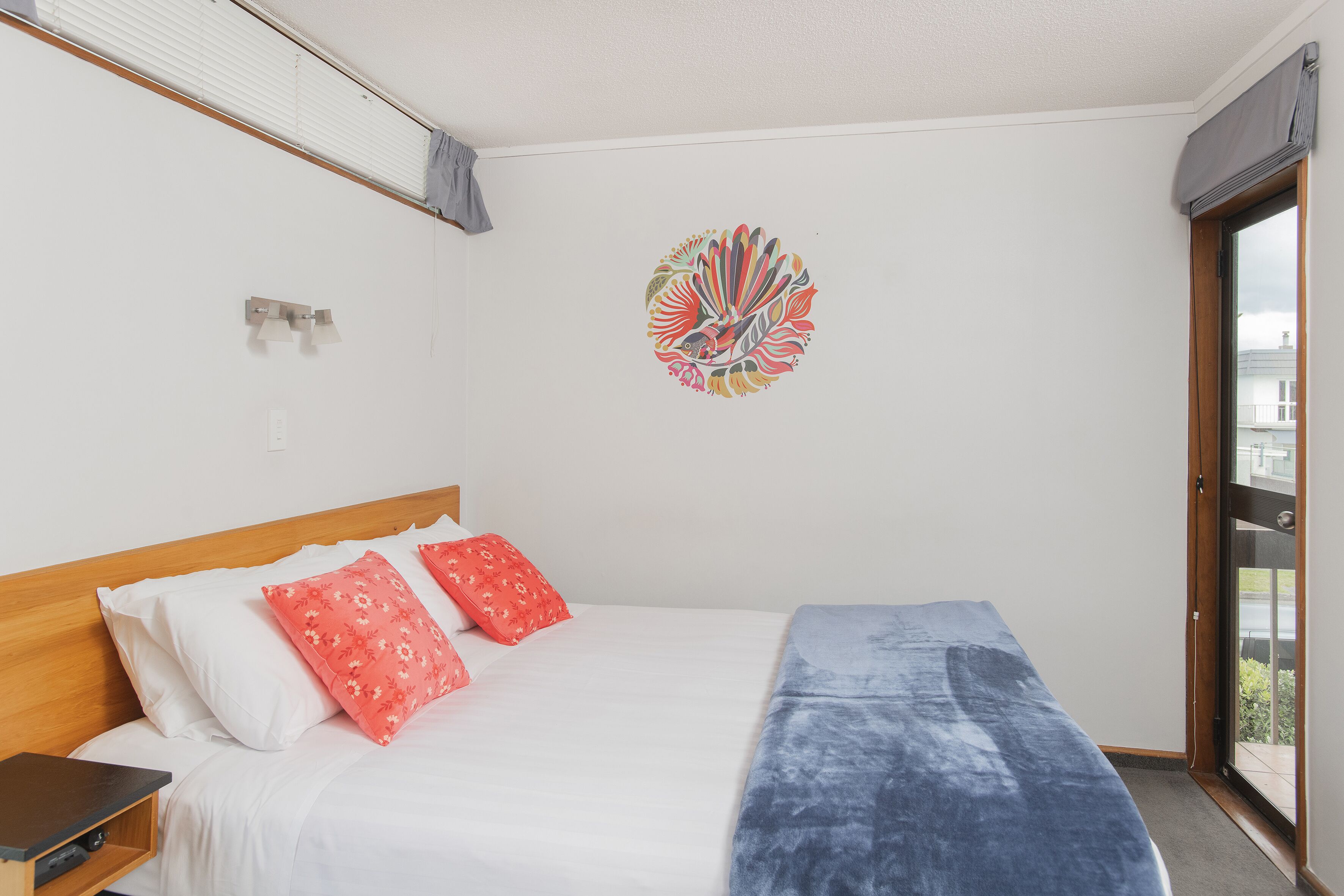 A bedroom with a bed, pillows, a wall art piece, and a window.