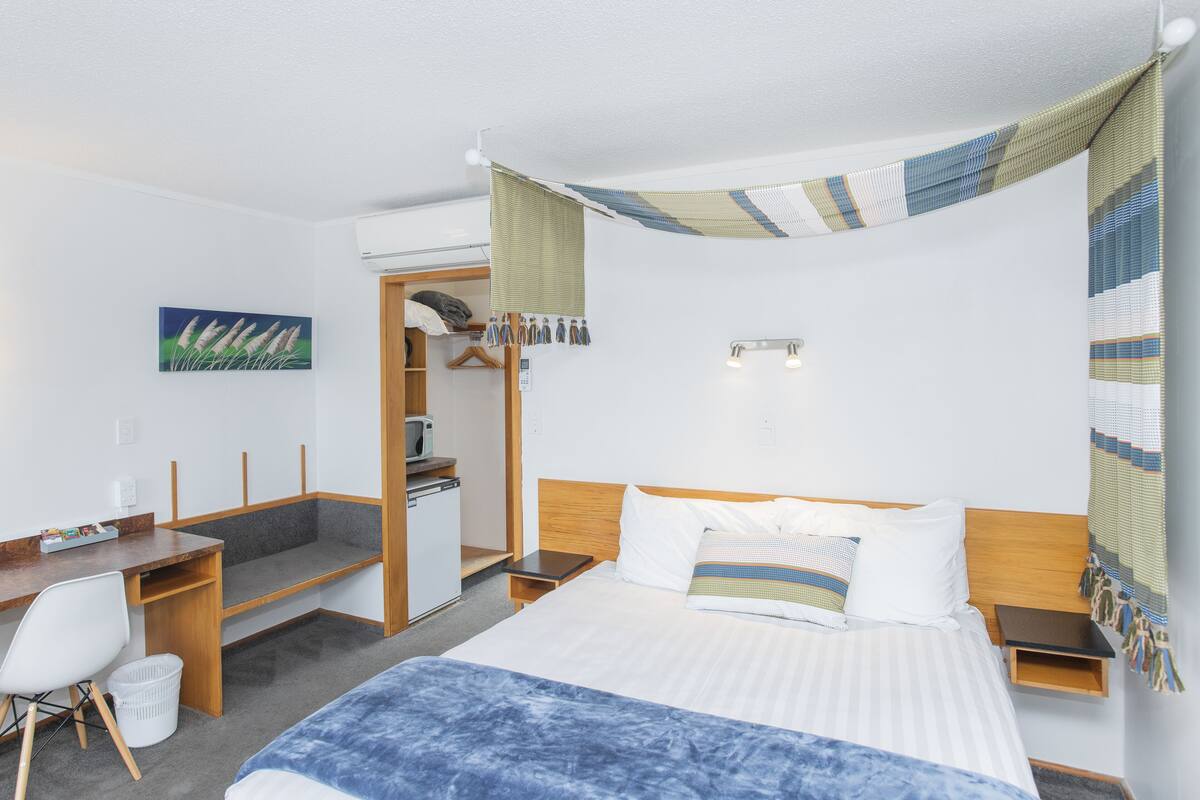 A hotel room with a bed, desk, chair, and a small kitchenette.