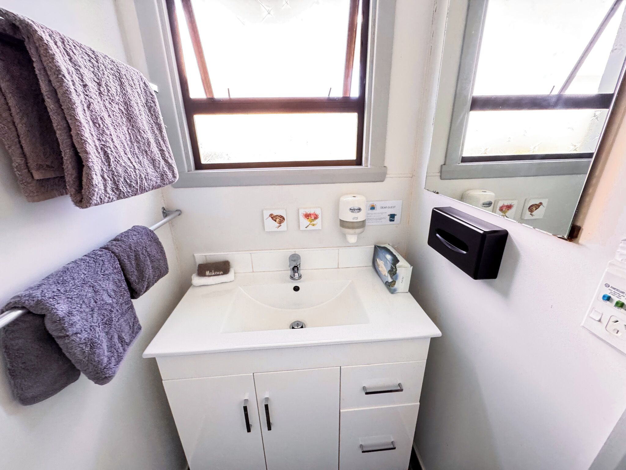 A bathroom with a sink, mirror, towel rack, and a window.
