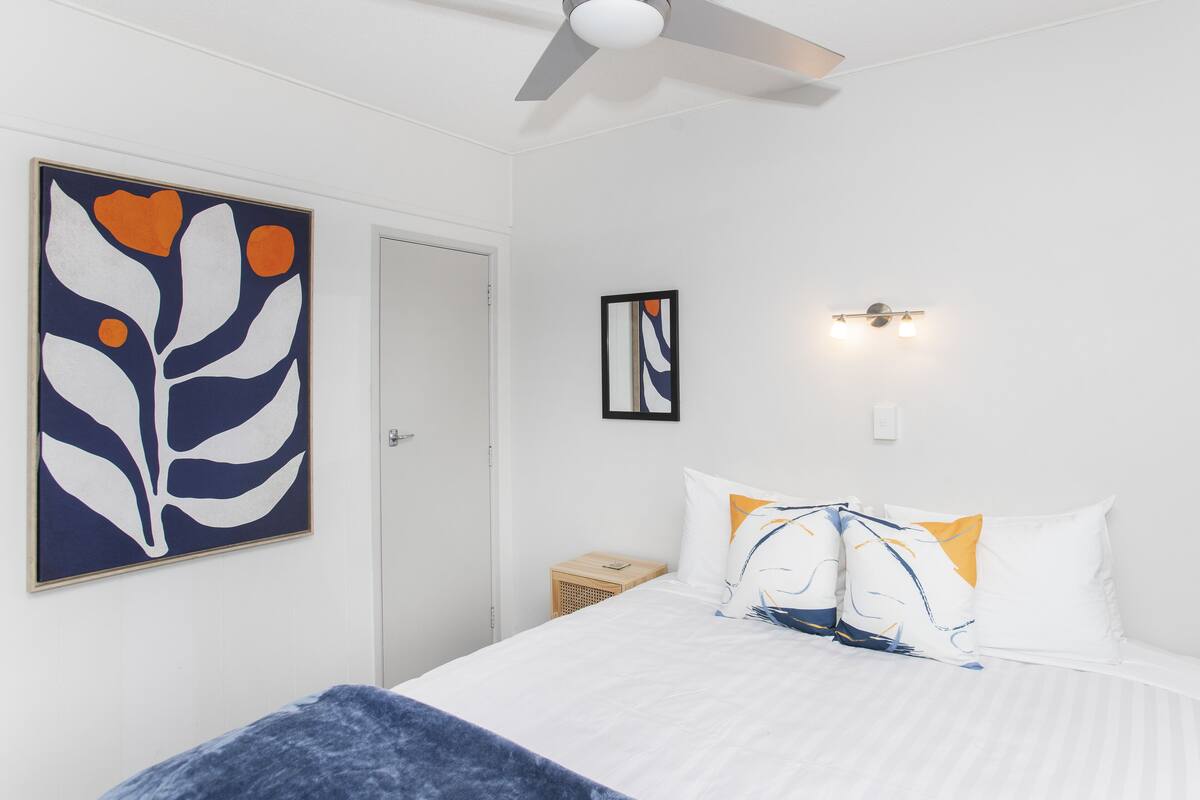 A bedroom with a bed, a ceiling fan, a wall-mounted light, and a door.