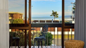 A balcony with a view of the ocean, a wicker chair, and a metal chair. - Waikanae Beach Motel (Gisborne)