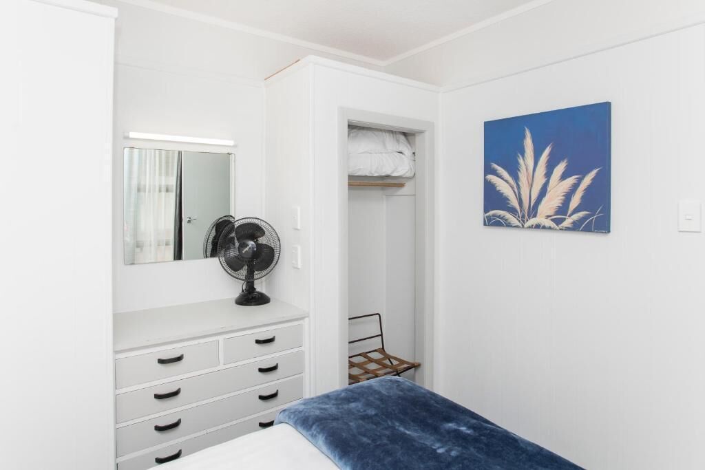 Quarto com cama, guarda-roupa, espelho, ventilador e um quadro na parede.