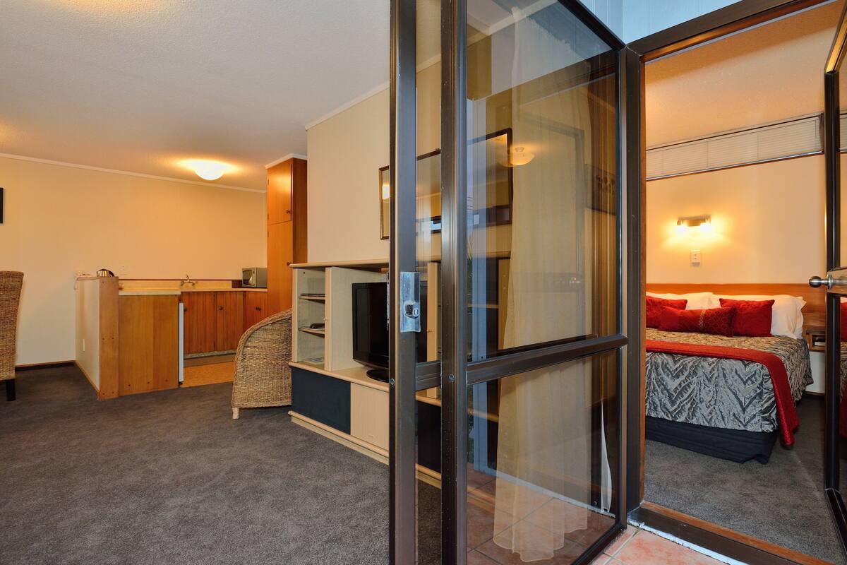 A hotel room with a bed, a television, a desk, and a sliding glass door leading to a balcony.