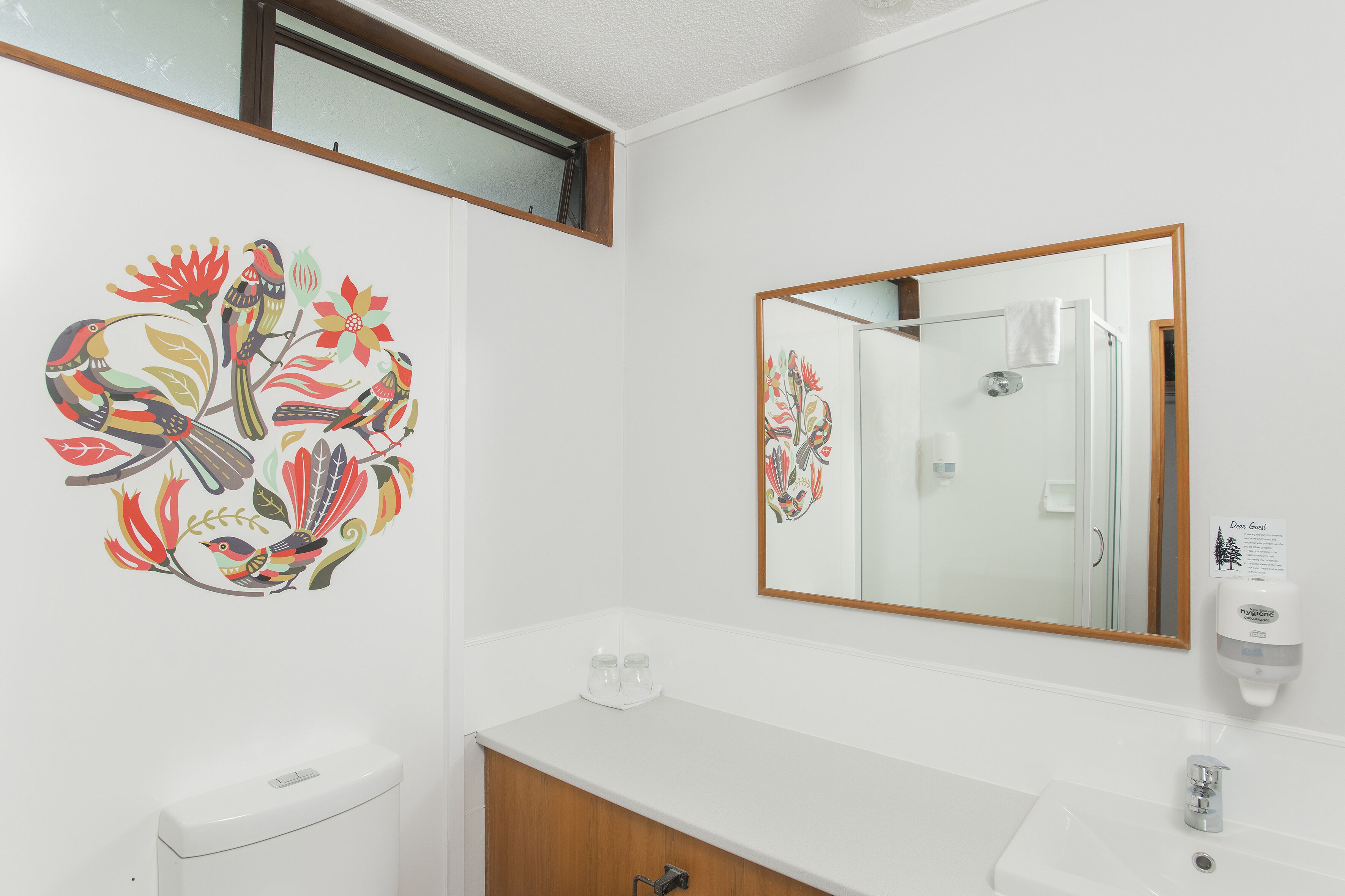 A bathroom with a white sink, a mirror, and a toilet. There is a decorative wall art of birds and flowers.