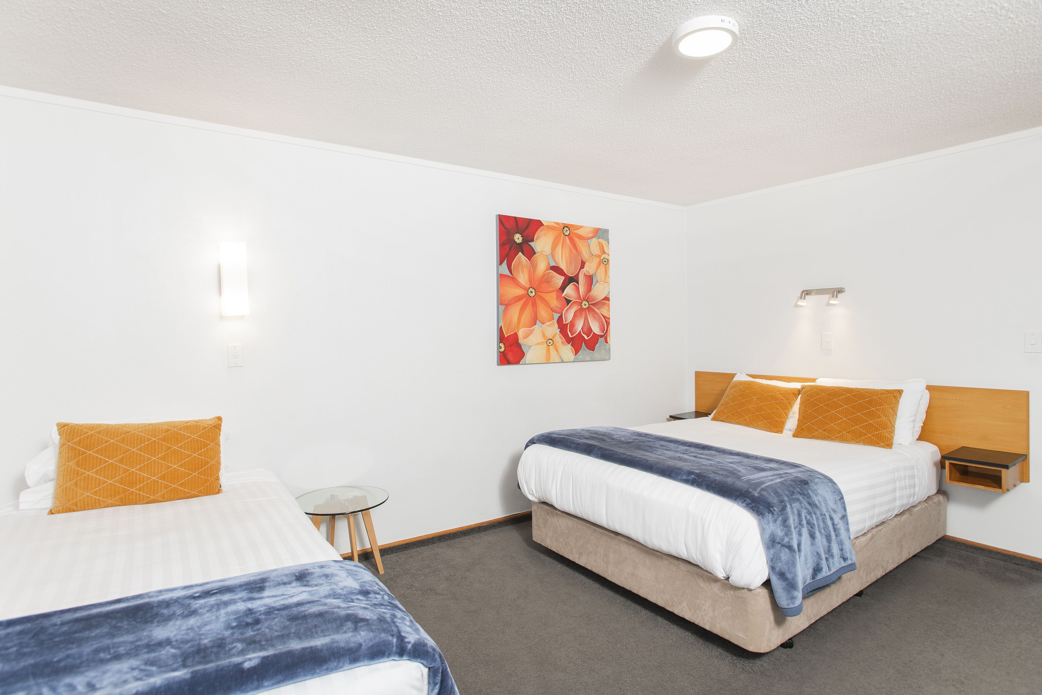 A hotel room with two beds, a small table, and a wall-mounted nightstand.