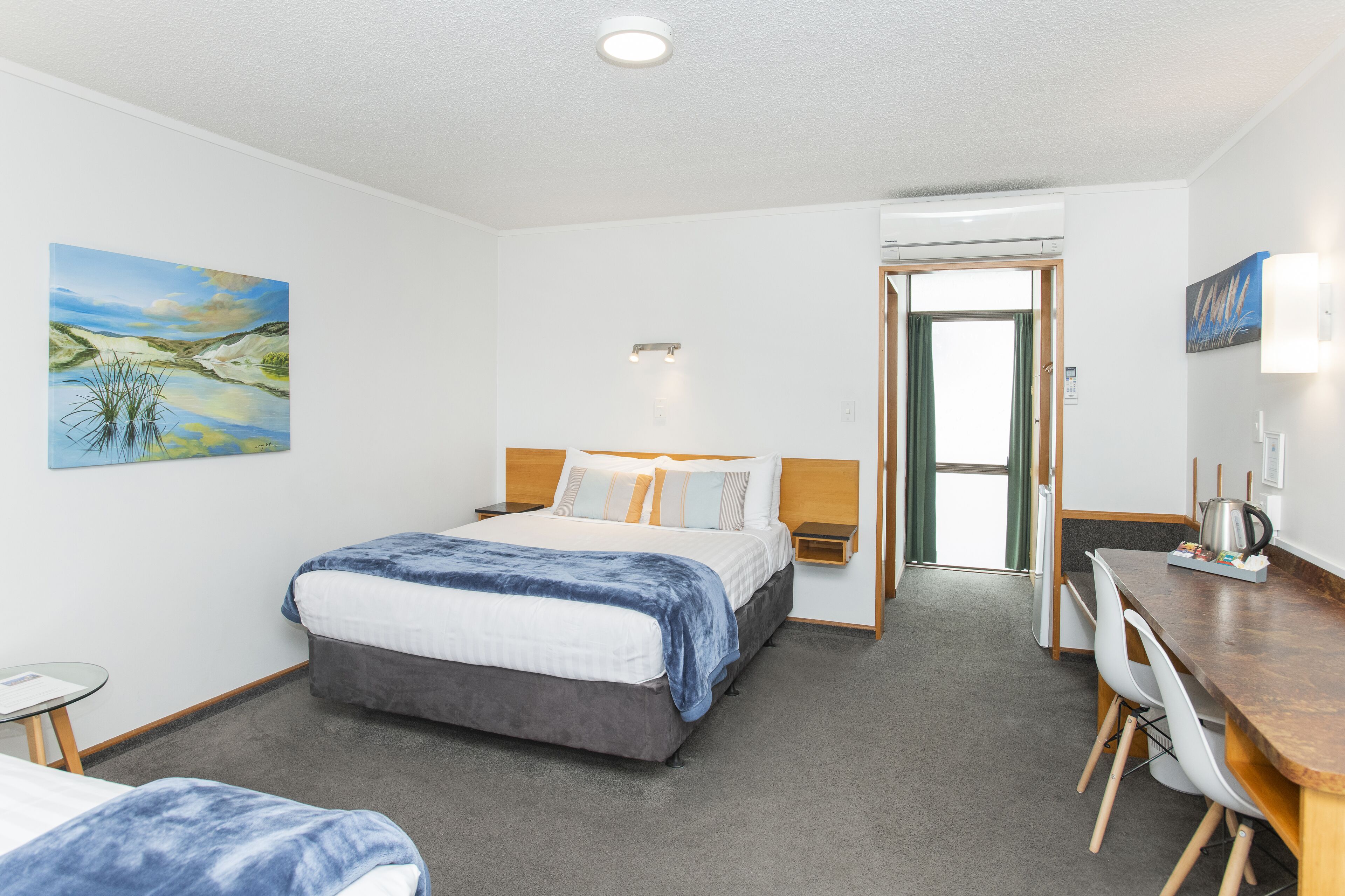 A hotel room with a bed, a desk, a chair, and a painting on the wall.