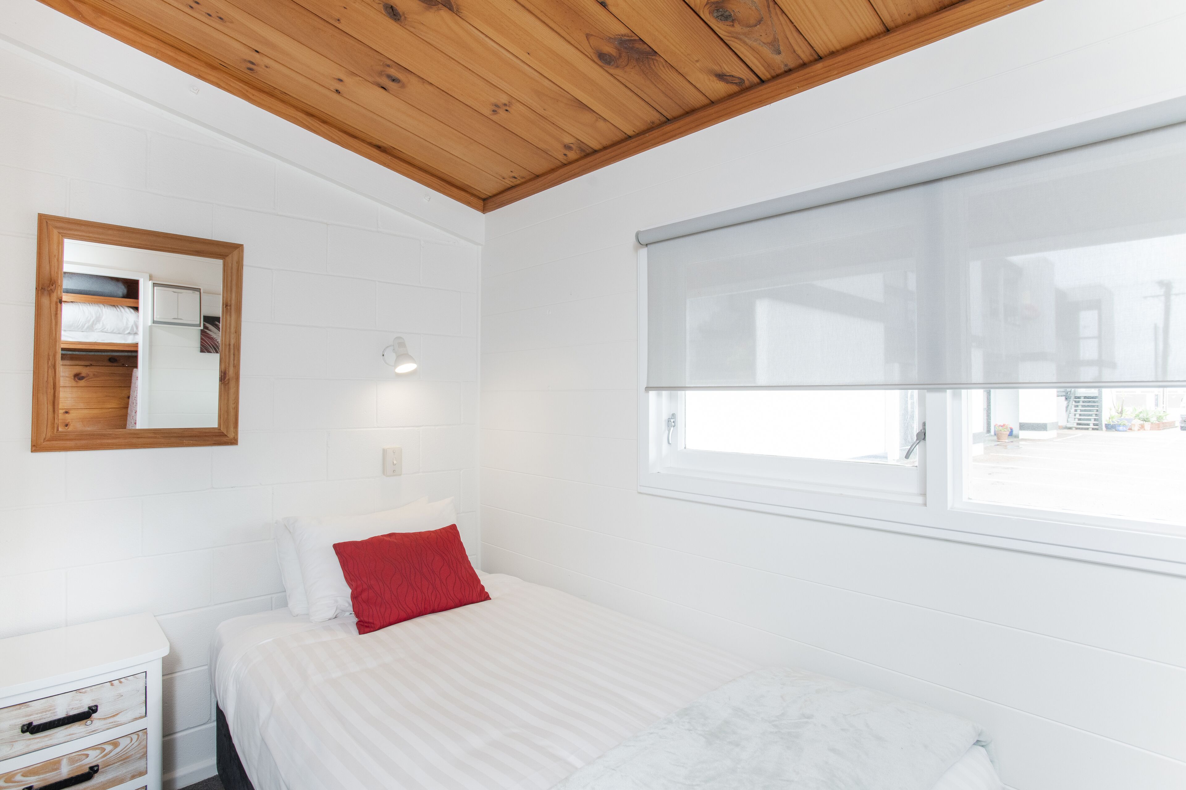 Un dormitorio con cama, mesita de noche, espejo y ventana.