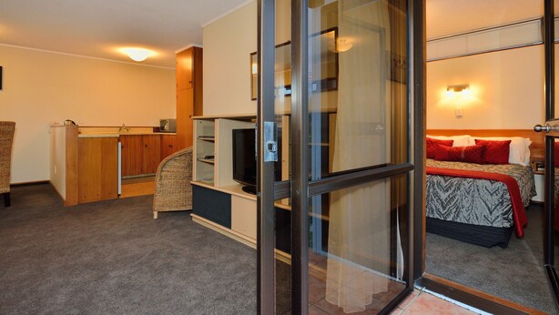 A hotel room with a bed, a television, a desk, and a sliding glass door leading to a balcony. - Waikanae Beach Motel (Gisborne)