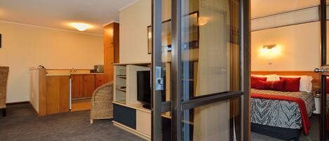 Habitación de hotel con cama, televisor, escritorio y puerta corrediza de vidrio que da a un balcón.