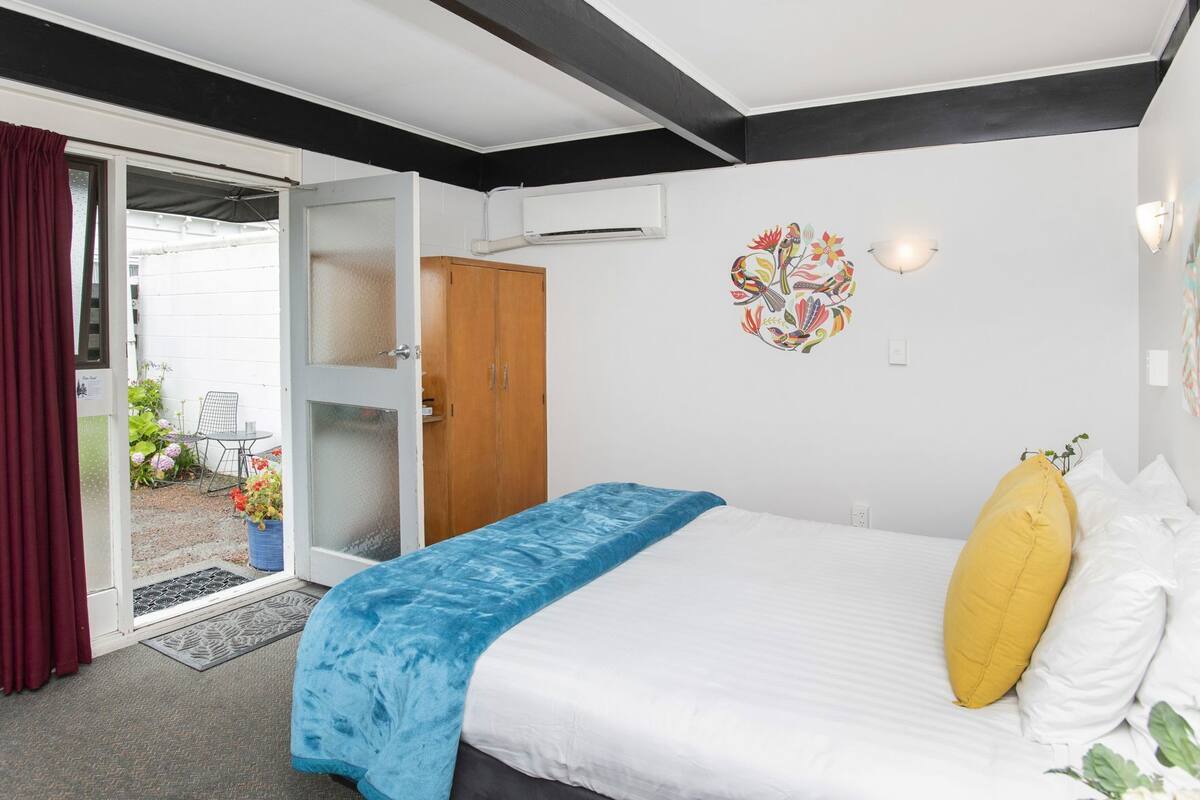 A bedroom with a bed, a wooden wardrobe, a door leading to a balcony, and a wall decoration.