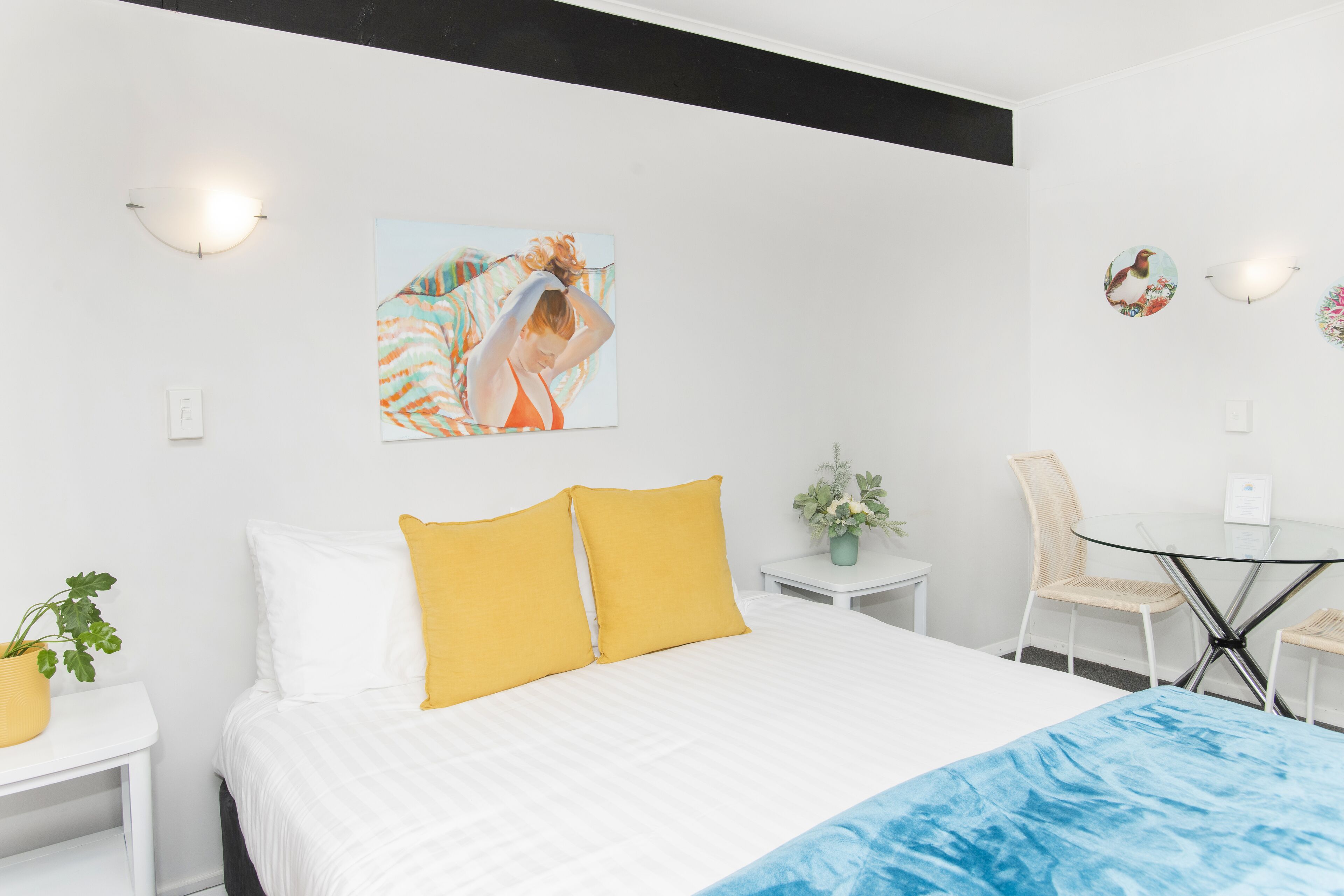 A hotel room with a bed, a small table, a chair, and a wall-mounted picture.