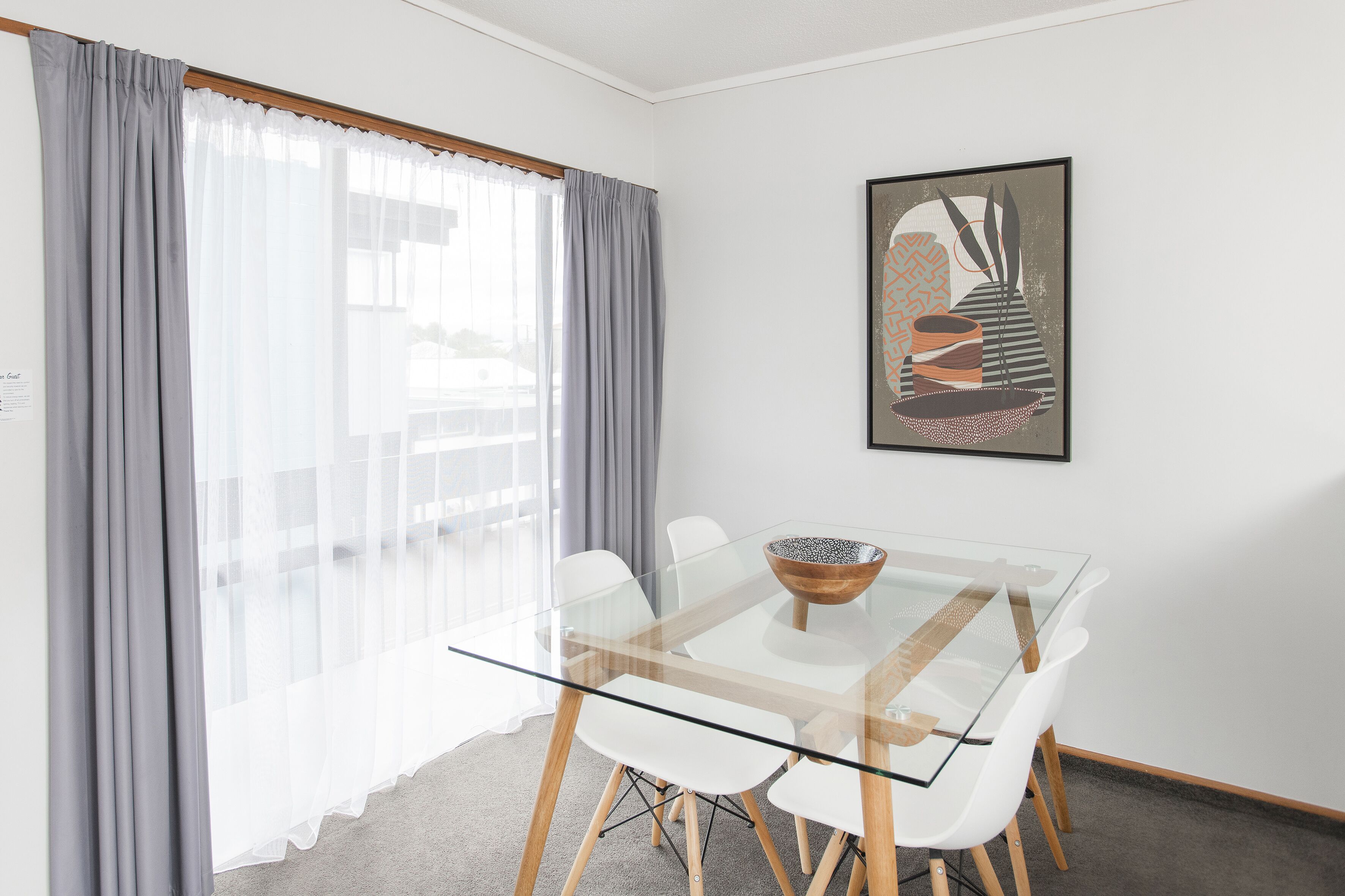 Un comedor moderno con una mesa de vidrio, sillas blancas y una cortina gris.