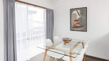 Un comedor moderno con una mesa de vidrio, sillas blancas y una cortina gris.
