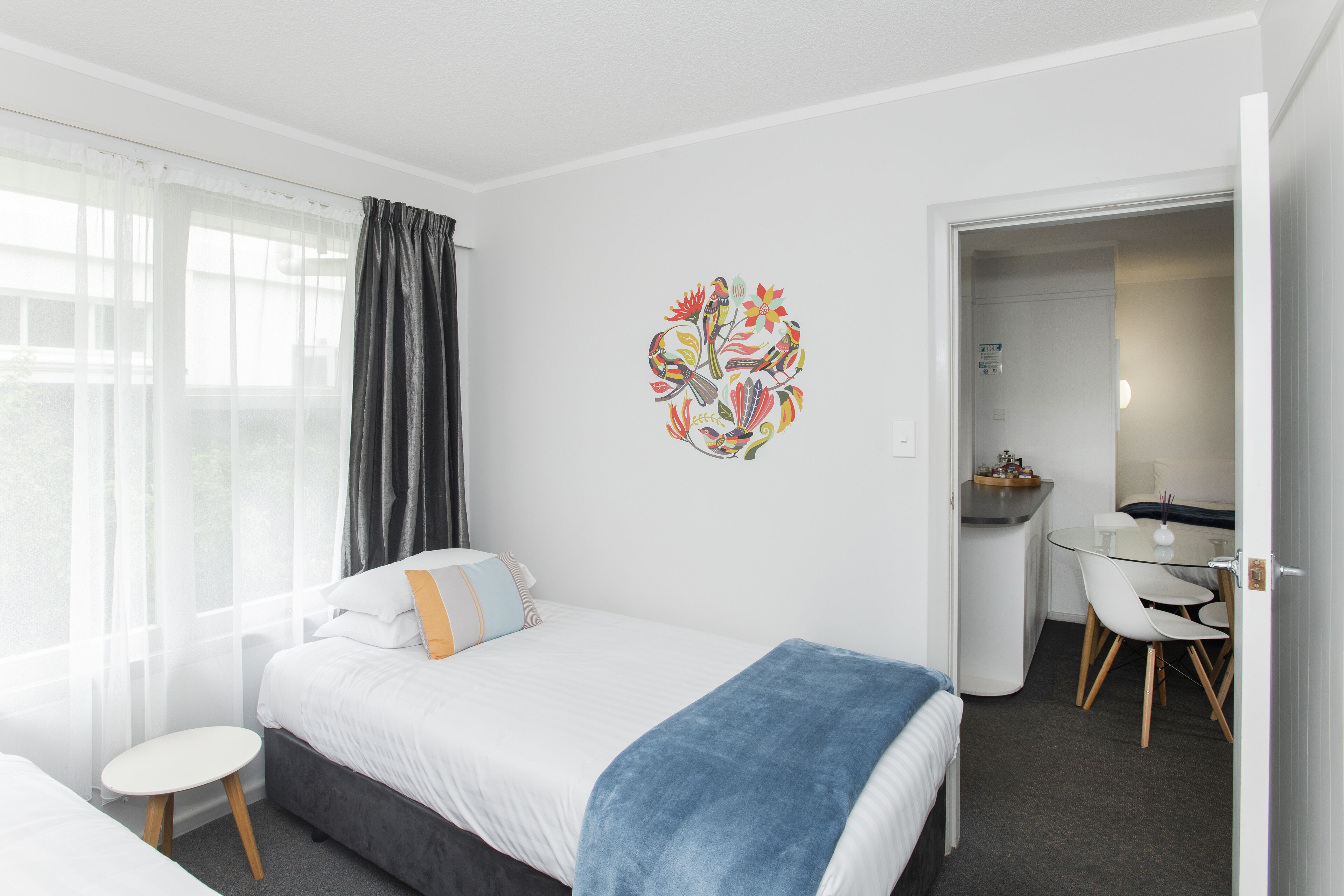 A modern hotel room with a bed, a small round table, and a desk with chairs.