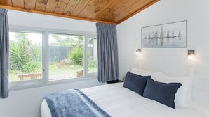 A bedroom with a bed, a window with curtains, a painting on the wall, and a view of greenery outside. - Waikanae Beach Motel (Gisborne)