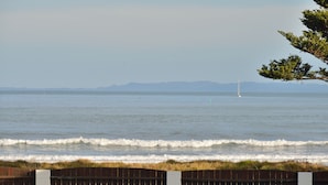 A coastal view with a wooden fence, a grassy area, and a distant sailboat on the water. - Waikanae Beach Motel (Gisborne)