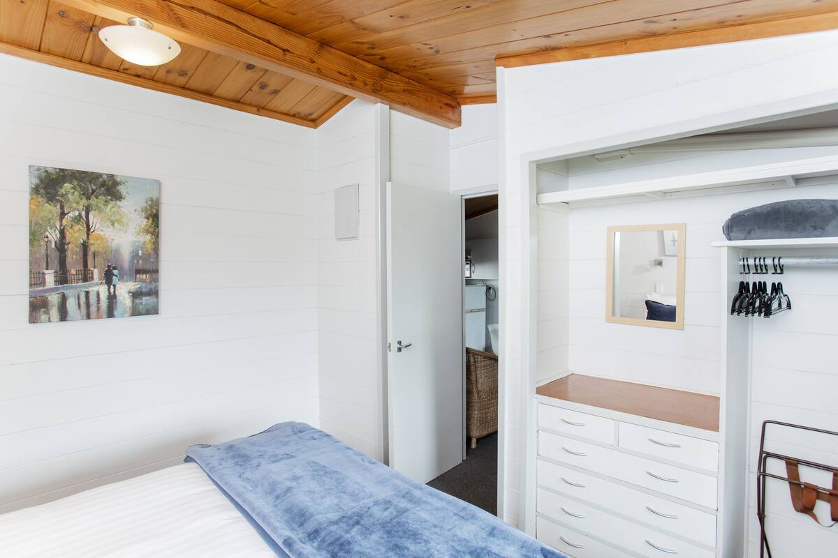 A bedroom with a bed, a dresser, a mirror, and a painting on the wall.
