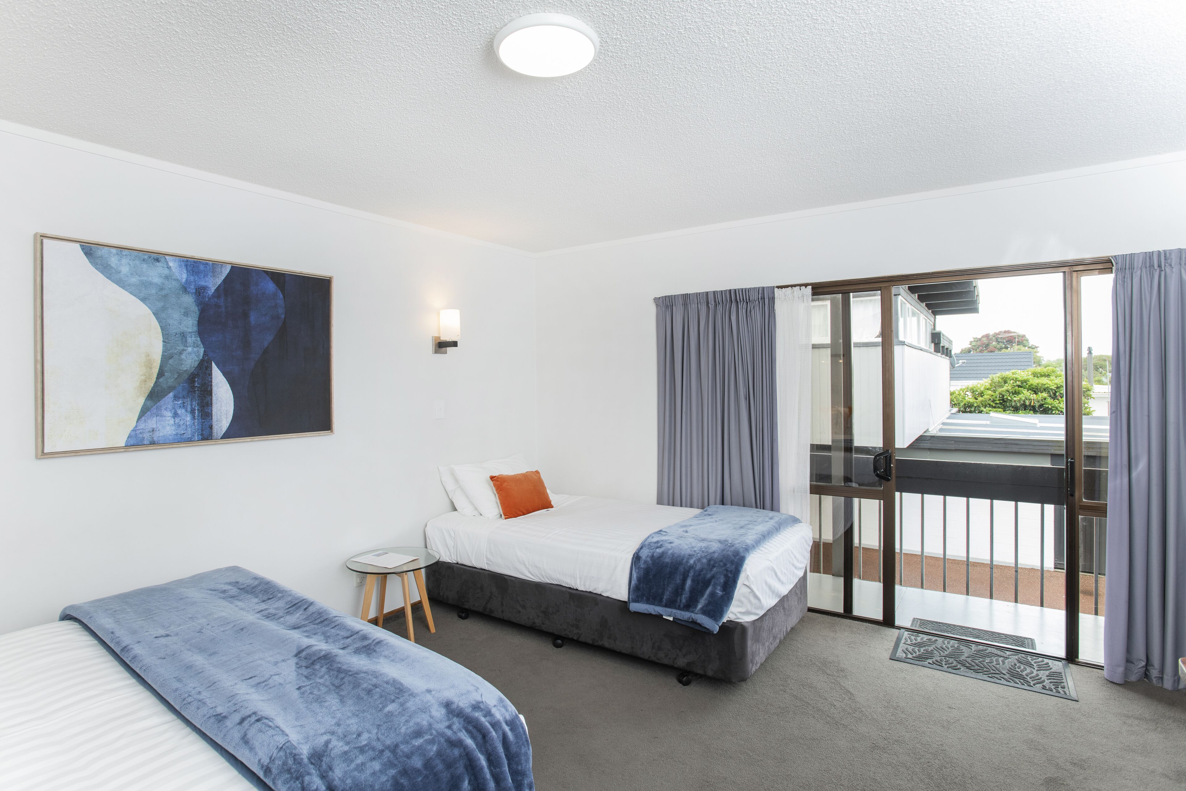 Ein Hotelzimmer mit Bett, einem kleinen Tisch, einem Sessel, einem Bild und Blick nach draußen.