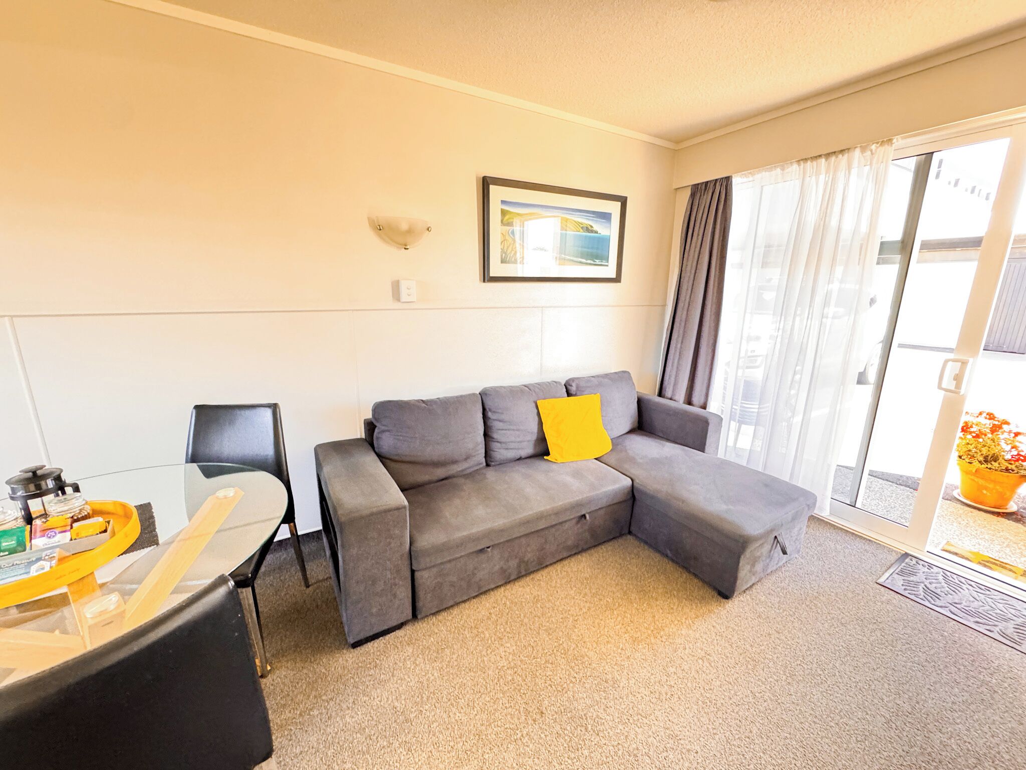 A modern living room with a grey sectional sofa, a small table with a yellow tray, and a window with curtains.