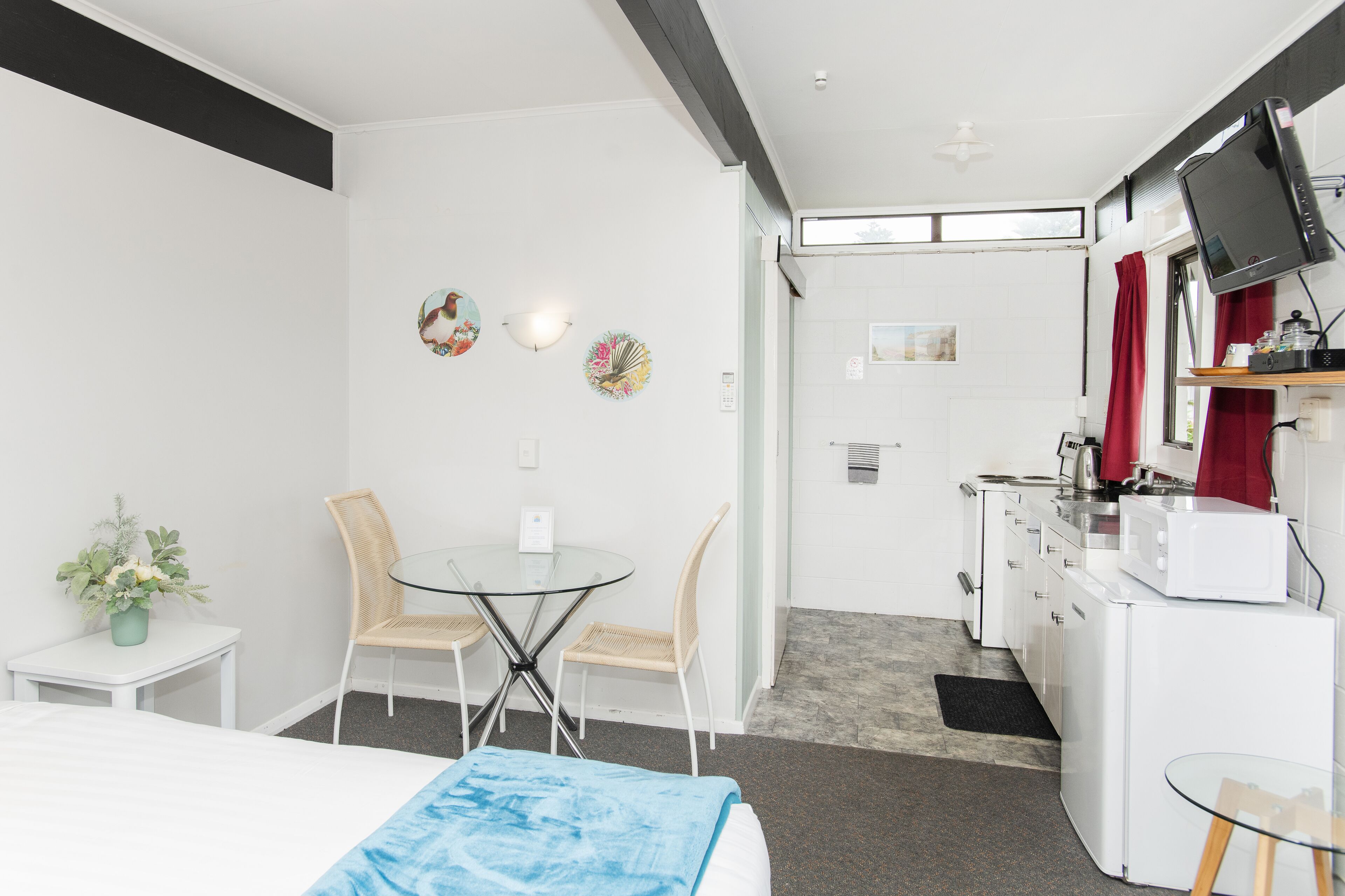 A hotel room with a bed, a small table with chairs, a kitchenette, and a TV mounted on the wall.