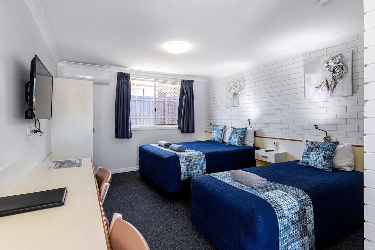 A hotel room with two beds, a desk, a TV, and a window with curtains.