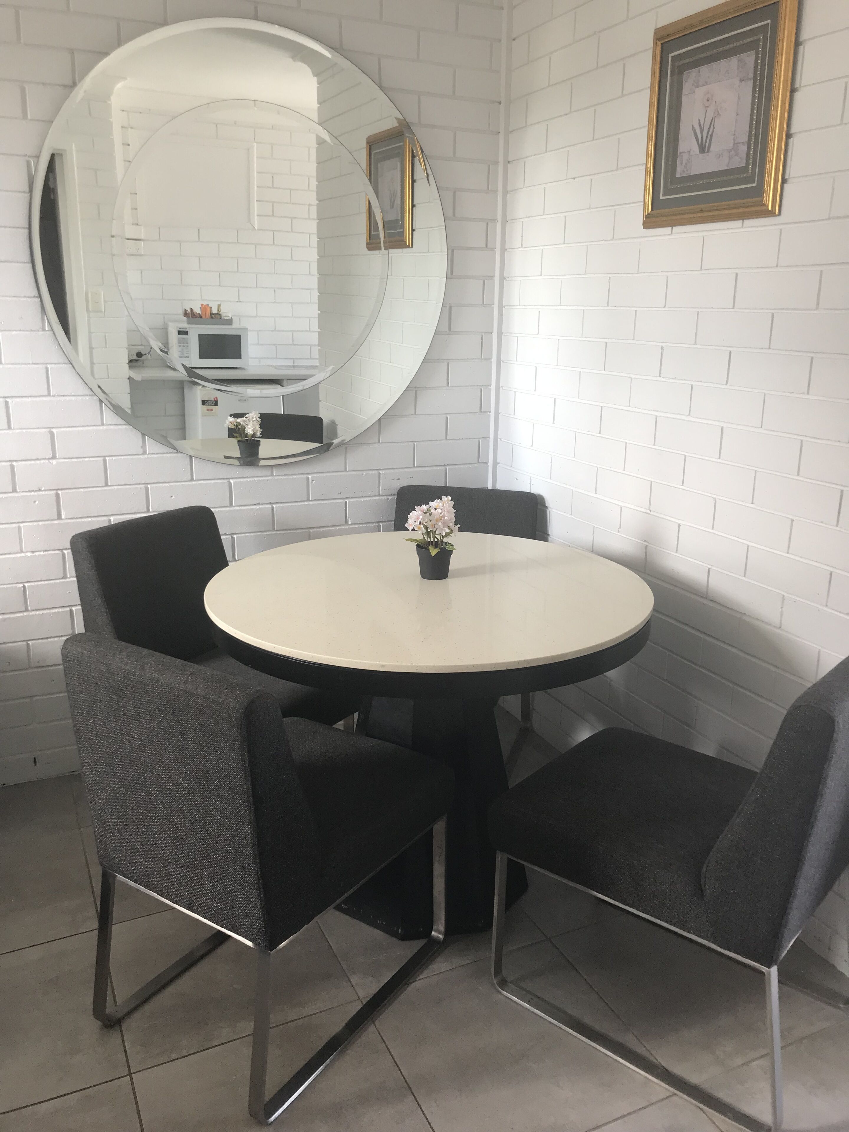Uma mesa redonda com quatro cadeiras, um espelho grande e um quadro emoldurado na parede.