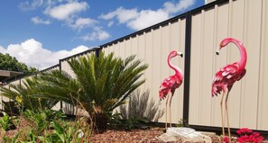 Twee roze flamingo standbeelden in een tuin met een palmboom en diverse planten.