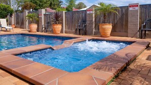 A rectangular swimming pool with a hot tub, surrounded by a wooden fence, potted plants, and a sign indicating a pool depth of 1m. - Leichhardt Motor Inn (South Toowoomba)