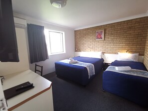 Een hotelkamer met twee bedden, een bureau, een stoel, een raam met gordijnen, een bakstenen muur en een schilderij.
