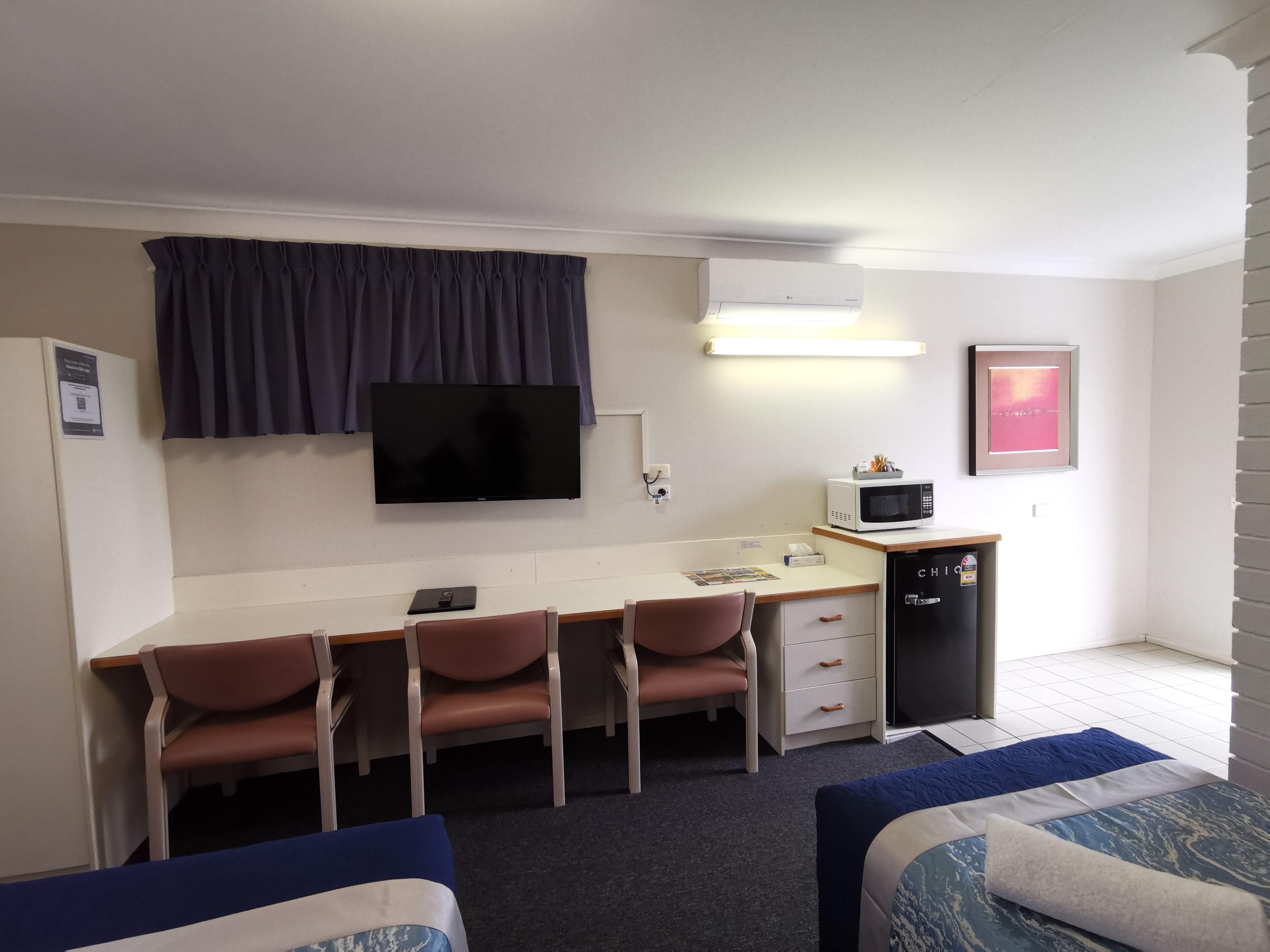 A room with a desk, two chairs, a television, a microwave, and a small cabinet.