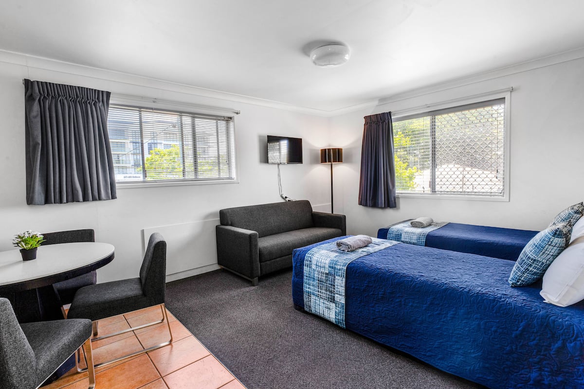A compact hotel room with a bed, a sofa, a small table, and a TV.