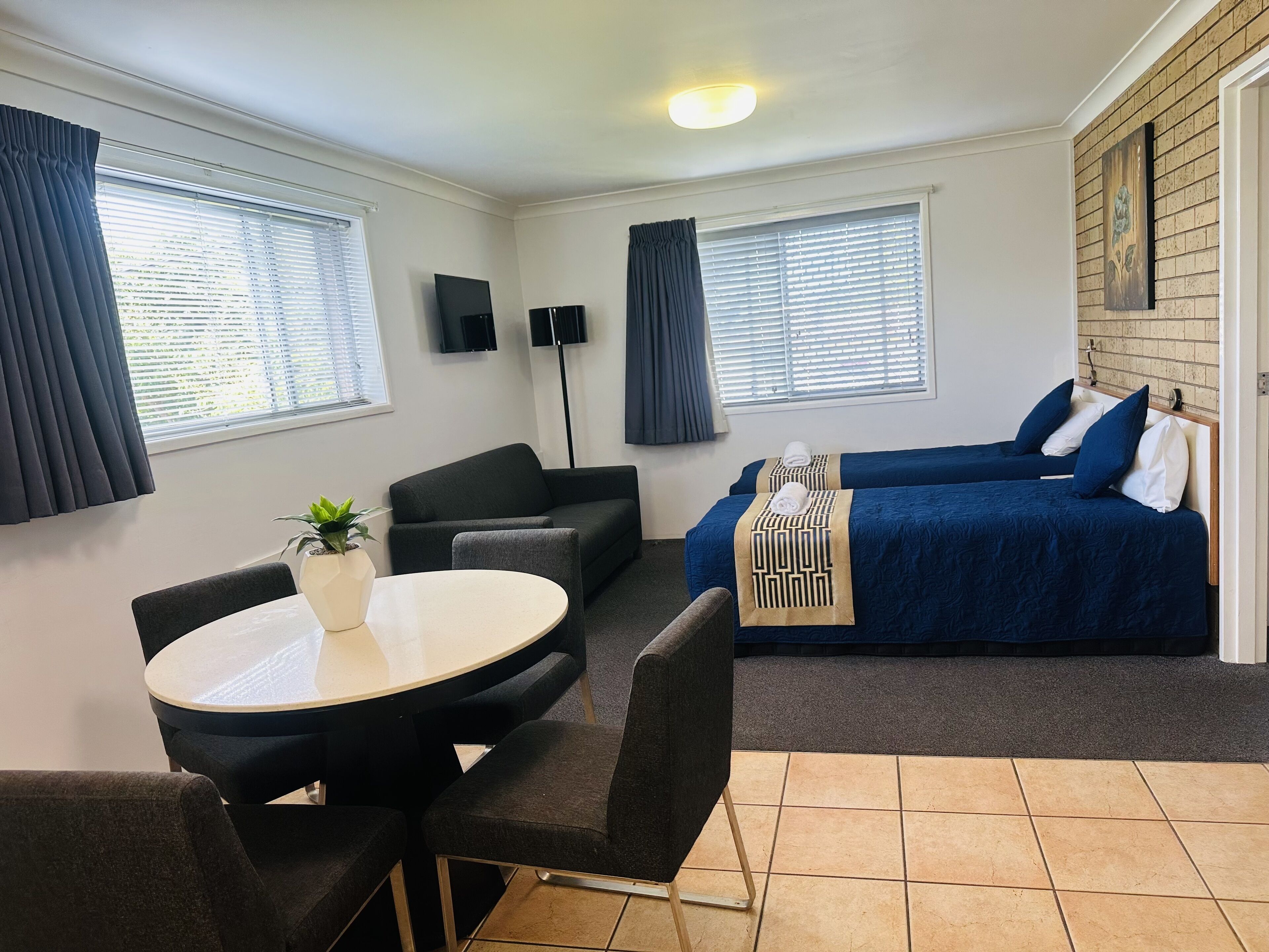 A compact hotel room with a sofa, two single beds, a small table, and a TV.