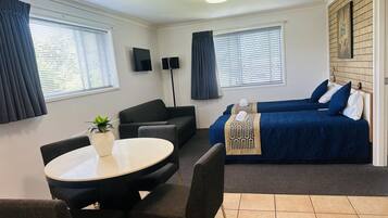 A compact hotel room with a sofa, two single beds, a small table, and a TV.